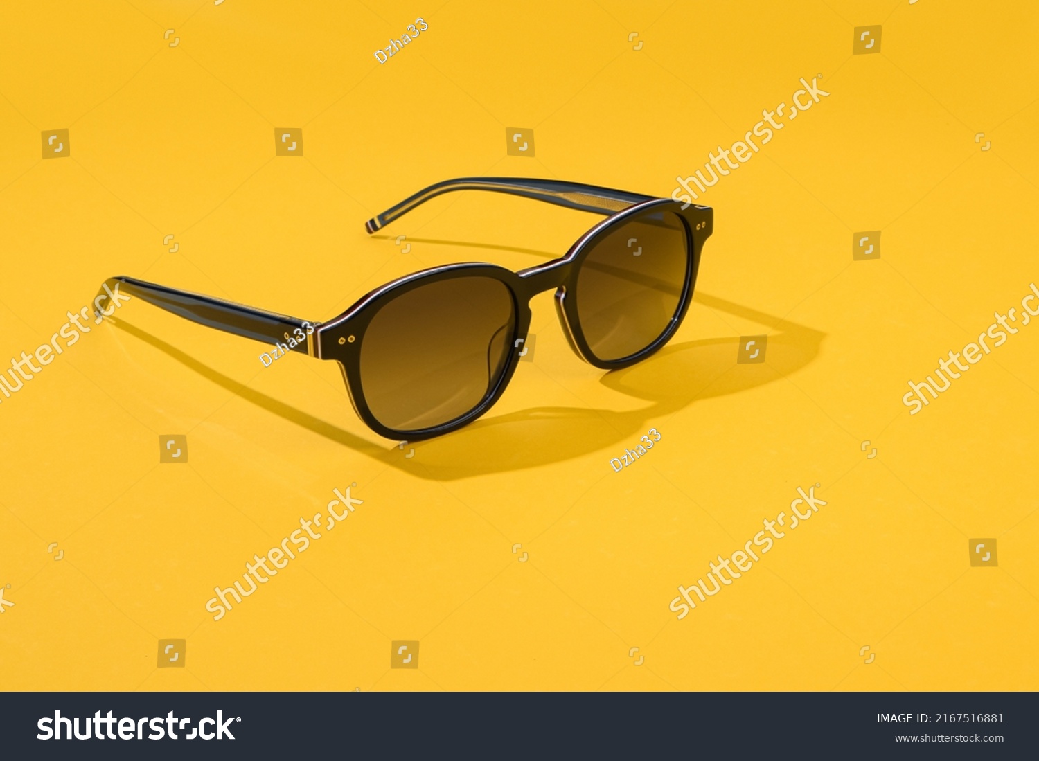 Black sunglass with oval frame, polarizing lenses. Sunglasses in beautiful fashion concept summer beach accessories. Sunglasses in sunlight on pastel blue color background. Front view #2167516881