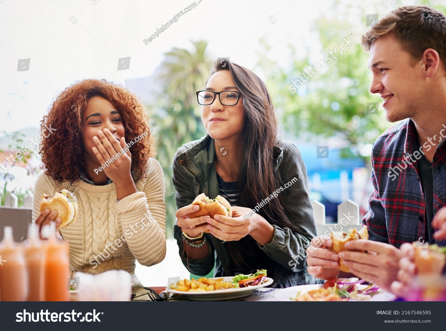Good food and laughter go hand-in-hand. Cropped shot of three friends eating burgers outdoors. #2167546595