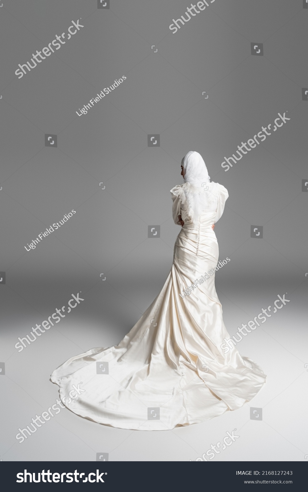 back view of muslim bride in gorgeous wedding dress standing on grey #2168127243