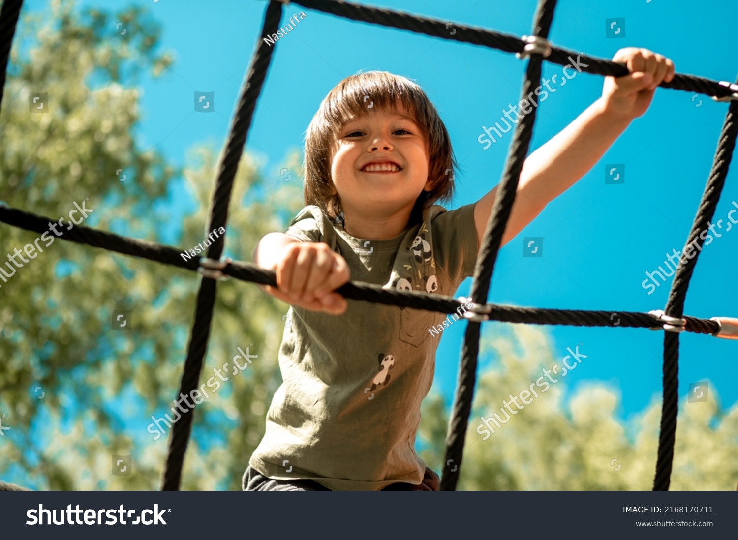 A child climbs up an alpine grid in a park on a playground on a hot summer day. children's playground in a public park, entertainment and recreation for children, mountaineering training. #2168170711