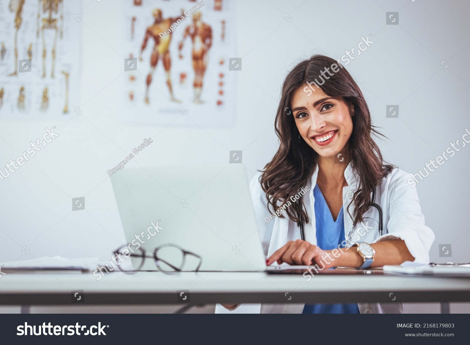Portrait of female doctor seating in her office at clinic. Friendly Latin American female doctor at the hospital looking at the camera and smiling. Confident female doctor at office desk #2168179803
