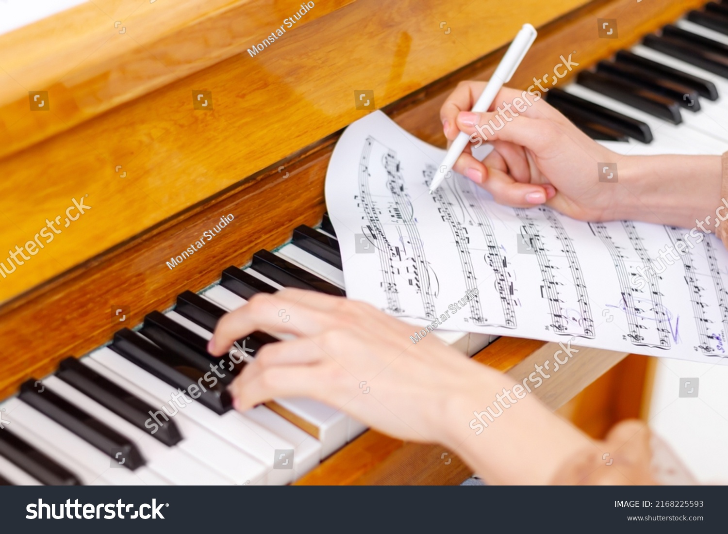 Woman's hands playing piano at home. The woman is professional pianist arranging music using piano keyboards. Musician practicing keyboard composing music. Artist create instrumental acoustic melody. #2168225593