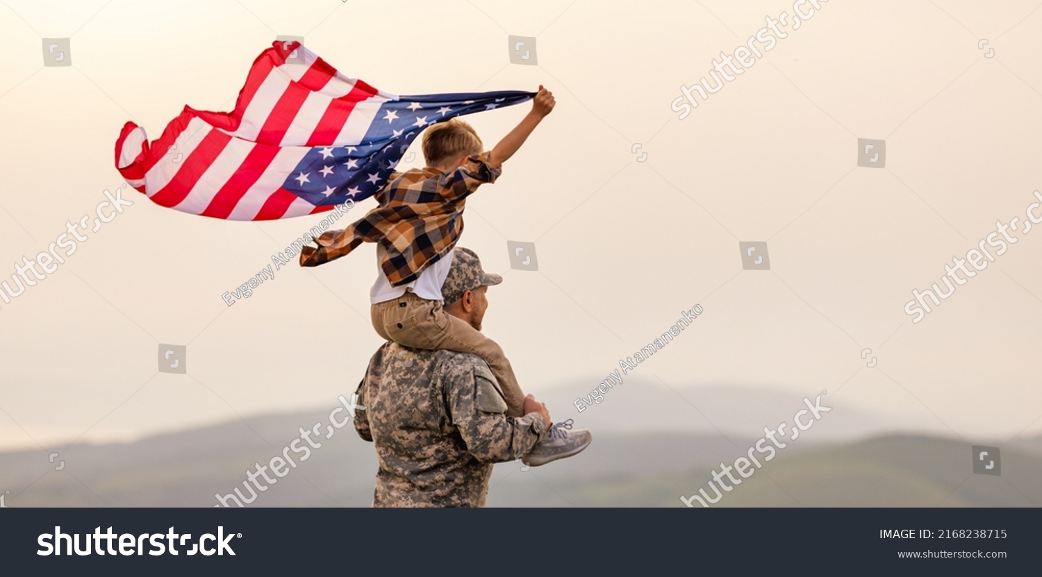 Military man father carrying happy little son with american flag on shoulders and enjoying amazing summer nature view on sunny day on July 4th, happy male soldier dad reunited with son after US army #2168238715