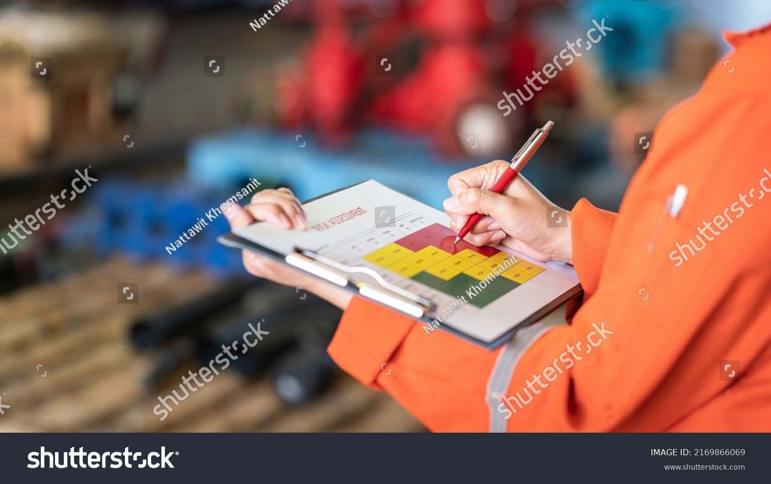 The manager is using ballpoint pen to marking on the risk assessment matrix at "High risk" level, with blurred background of factory place. Industrial and business working photo. #2169866069