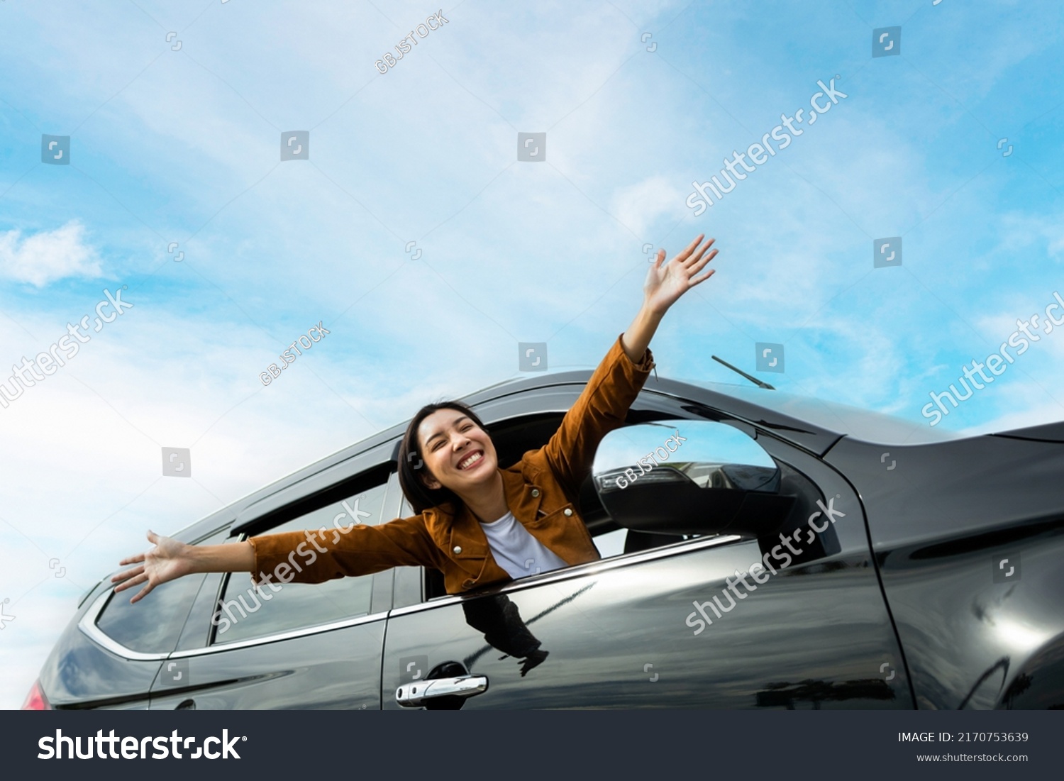 Young beautiful asian women getting new car. she very happy and excited. Smiling female driving vehicle on the road on a bright day. Sticking her head outta the windshield #2170753639