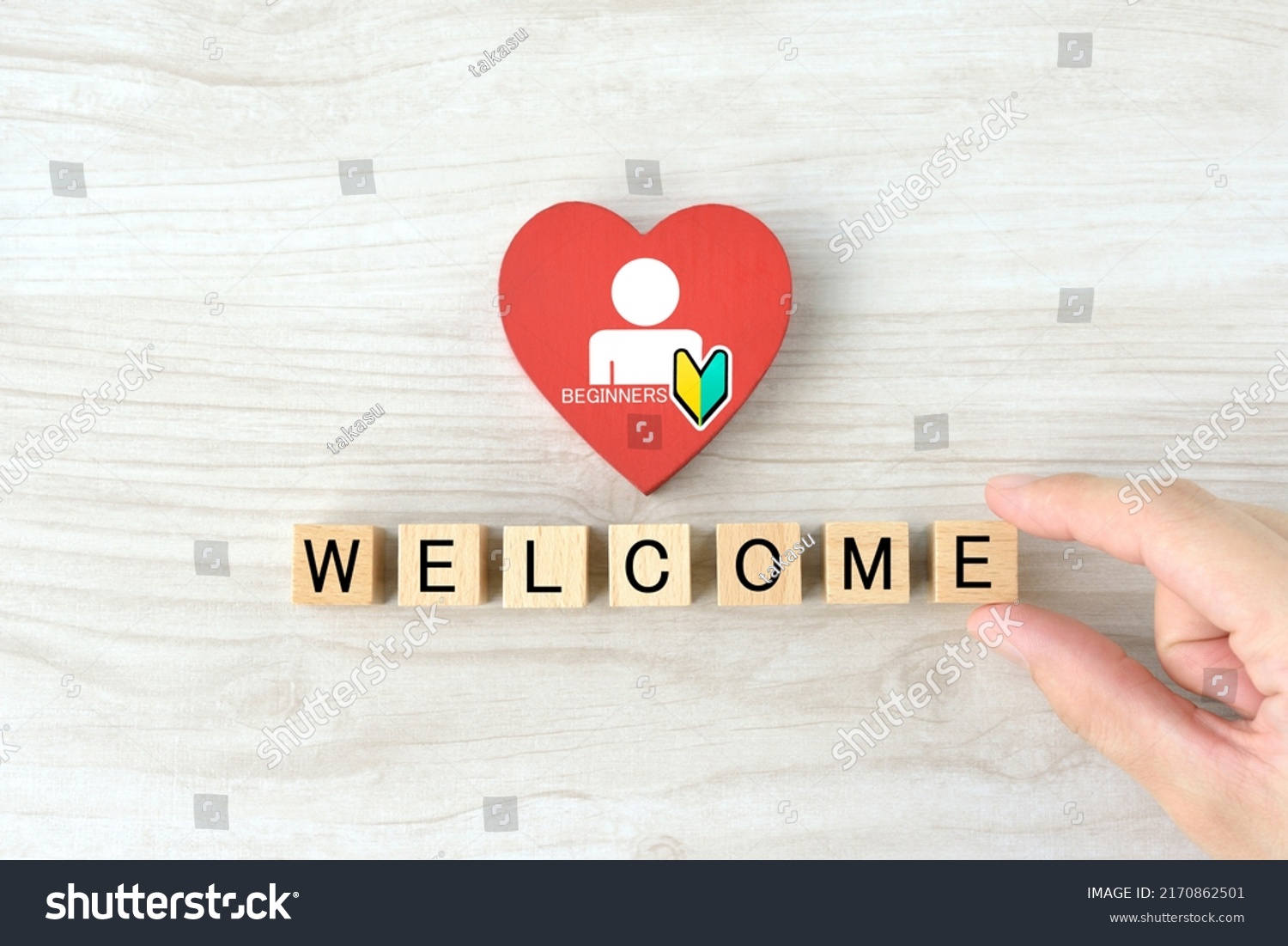 Businessman's hand with human pictogram and Japanese beginners mark drawn on heart object and wooden blocks with "WELCOME" word #2170862501