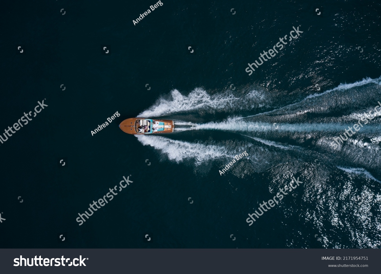 Modern wooden boat in a classic design, moving on water, aerial view. Luxurious wooden boat with people moves on dark water top view. Italian classic wooden boat fast movement on the water top view. #2171954751