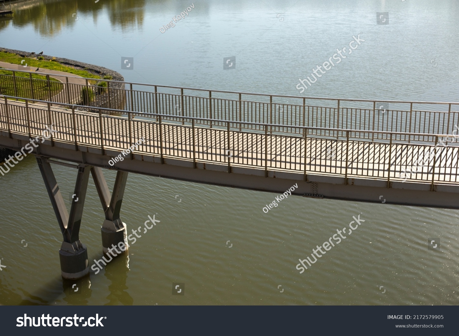 Pedestrian bridge on water. Bridge with railings. Details of park in city. Embankment on lake. #2172579905