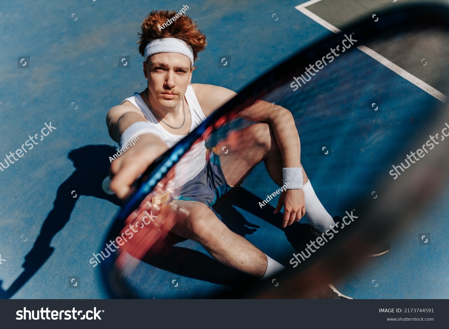 Portrait of a healthy athletic man in retro style with an athletic build with a tennis racket. Redhead guy playing tennis on the sports ground. Portrait of a healthy athletic man with an  #2173744591