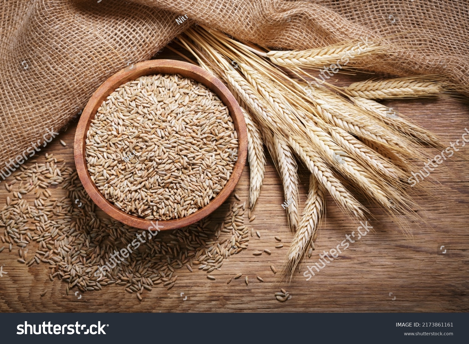 Bowl of rye grains and ears on wooden table, top view #2173861161