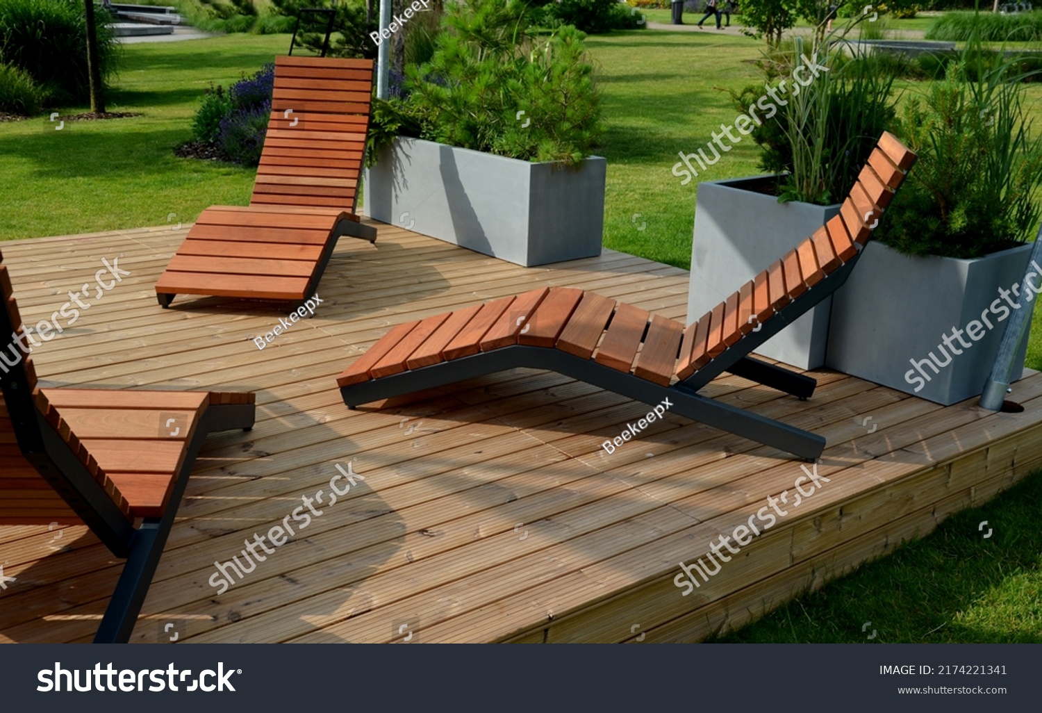 rocking chair on the pavement under the trees in the square. wooden deck chairs made of tropical wood for one person in the park. They are comfortable made of brown planks, slats steel frames, pine #2174221341