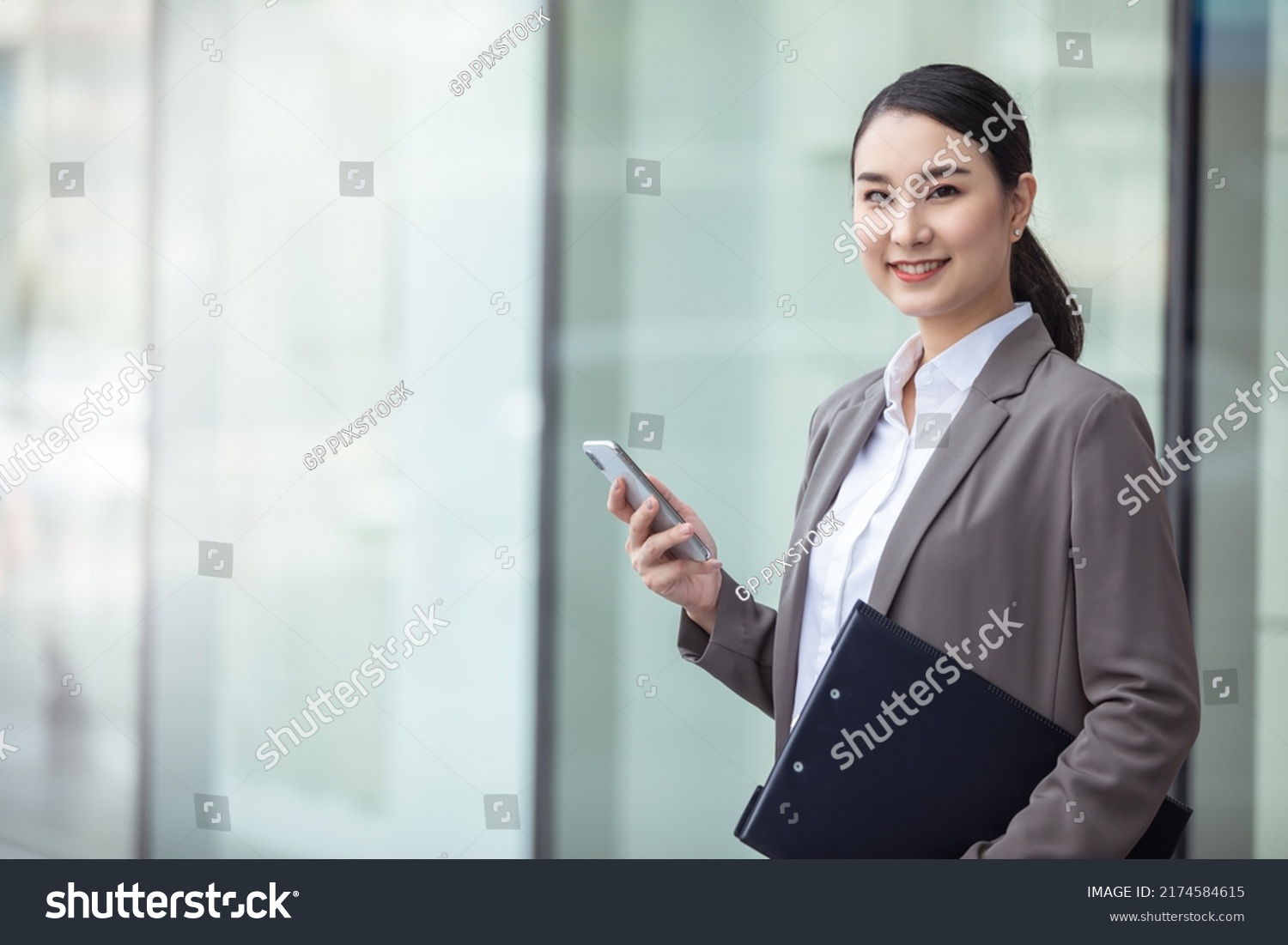 Asian woman with smartphone standing against street blurred building background, asian business photo of beautiful girl in casual suite with smart phone.  #2174584615