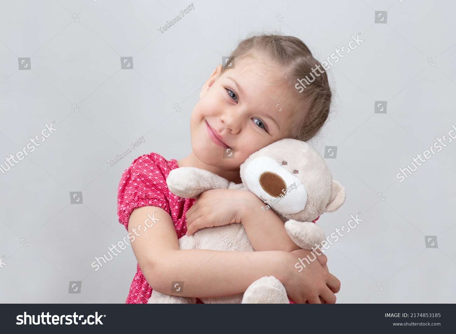 Happy child hugging teddy bear on white background caucasian little girl of 5-6 years in red looking at camera #2174853185
