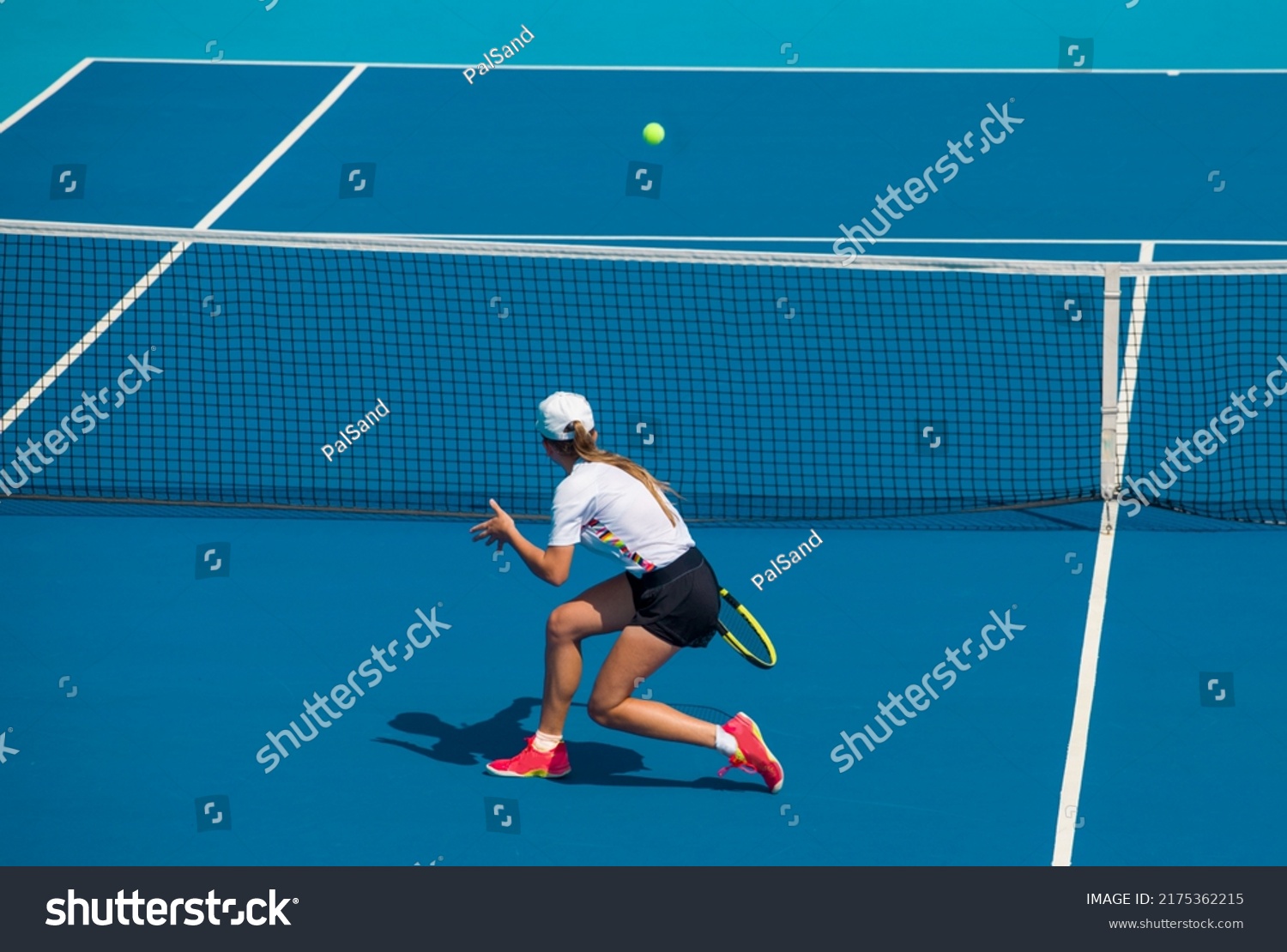 A girl plays tennis on a court with a hard blue surface on a summer sunny day #2175362215