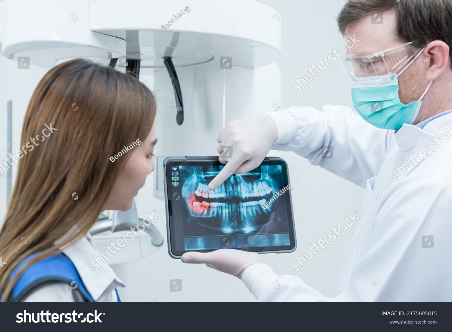 Caucasian male dentist hold digital tablet and explaining tooth problem. Caucasian male doctor use tablet and giving advice or consultation to Asian young girl patient about oral care in dental clinic #2175605815