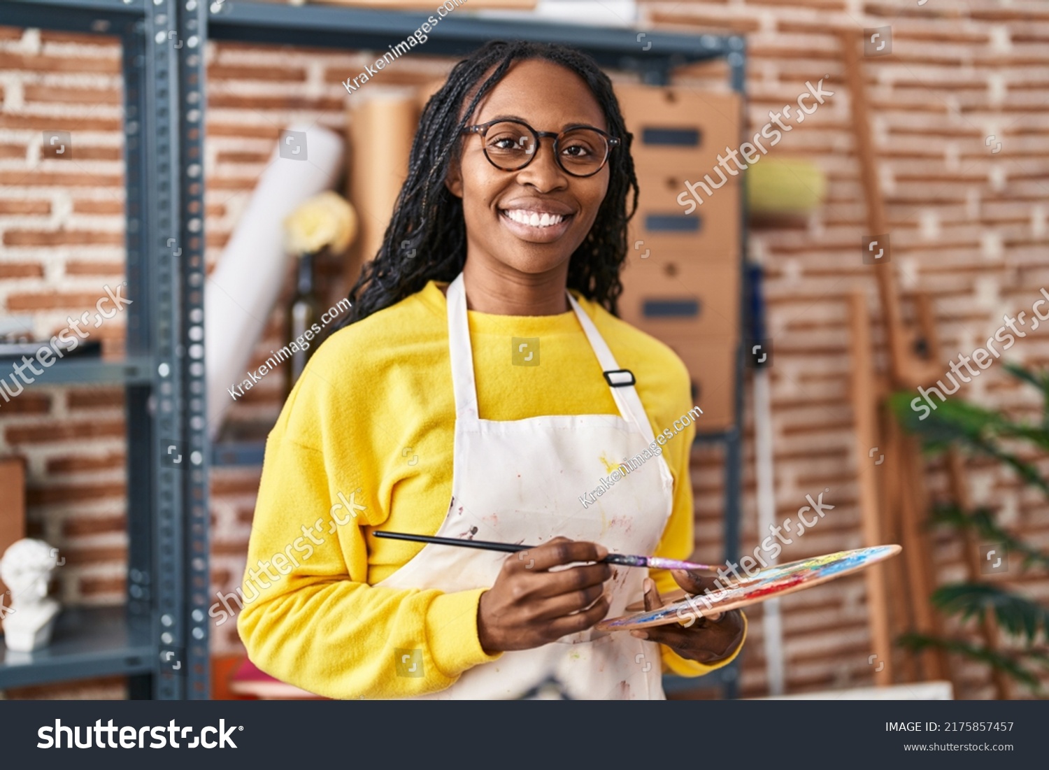 African american woman artist smiling confident holding paintbrush and palette at art studio #2175857457