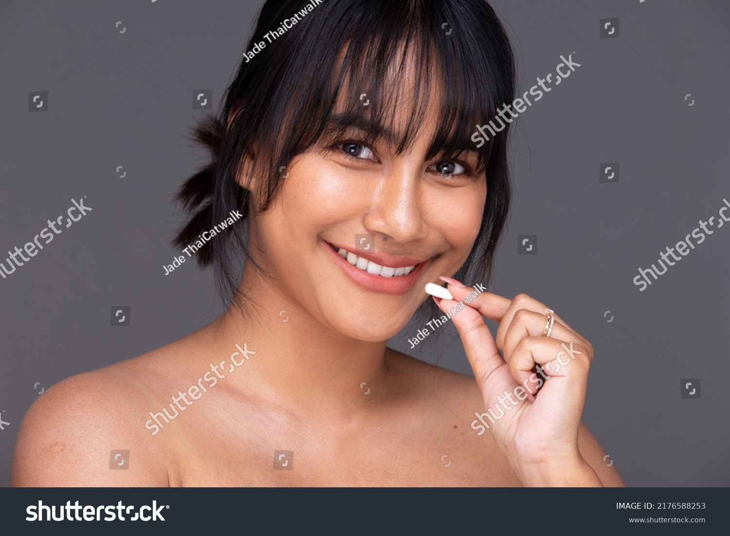 Asian Indian woman show beautiful smile happy lips, hold empty blank package capsule for treatment skin care. India Female feel wellbeing with medicine capsule in studio over gray background isolated #2176588253