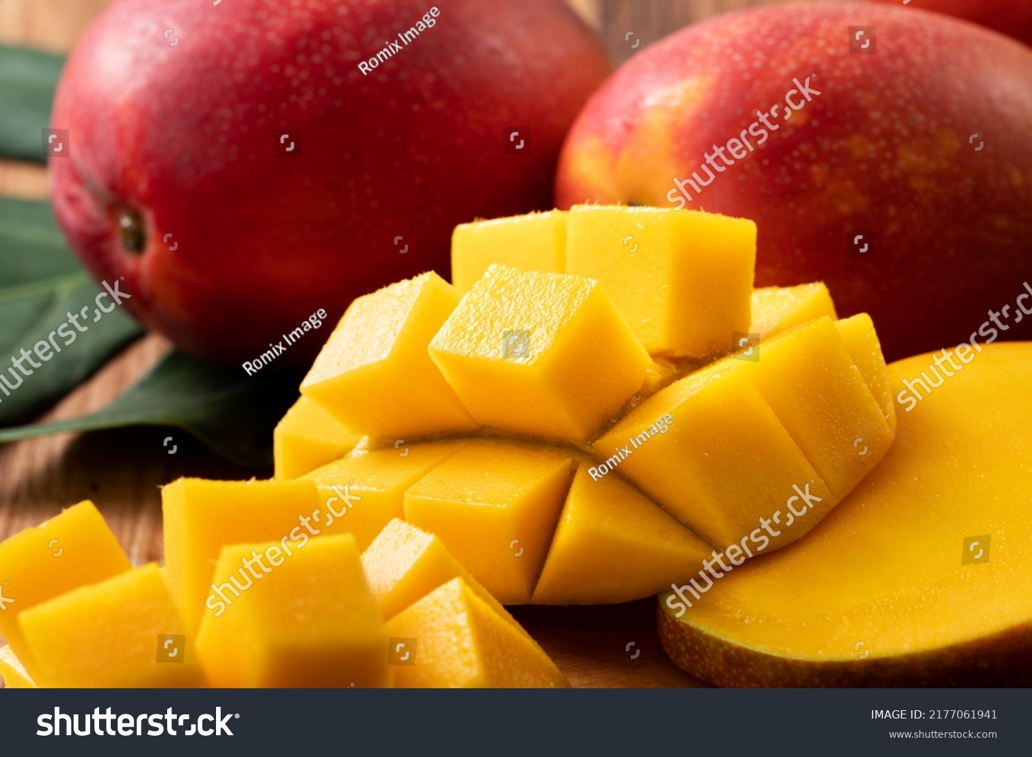 Mango. Close up of fresh ripe mango fruit with leaves over dark wooden table background with green leaves. #2177061941