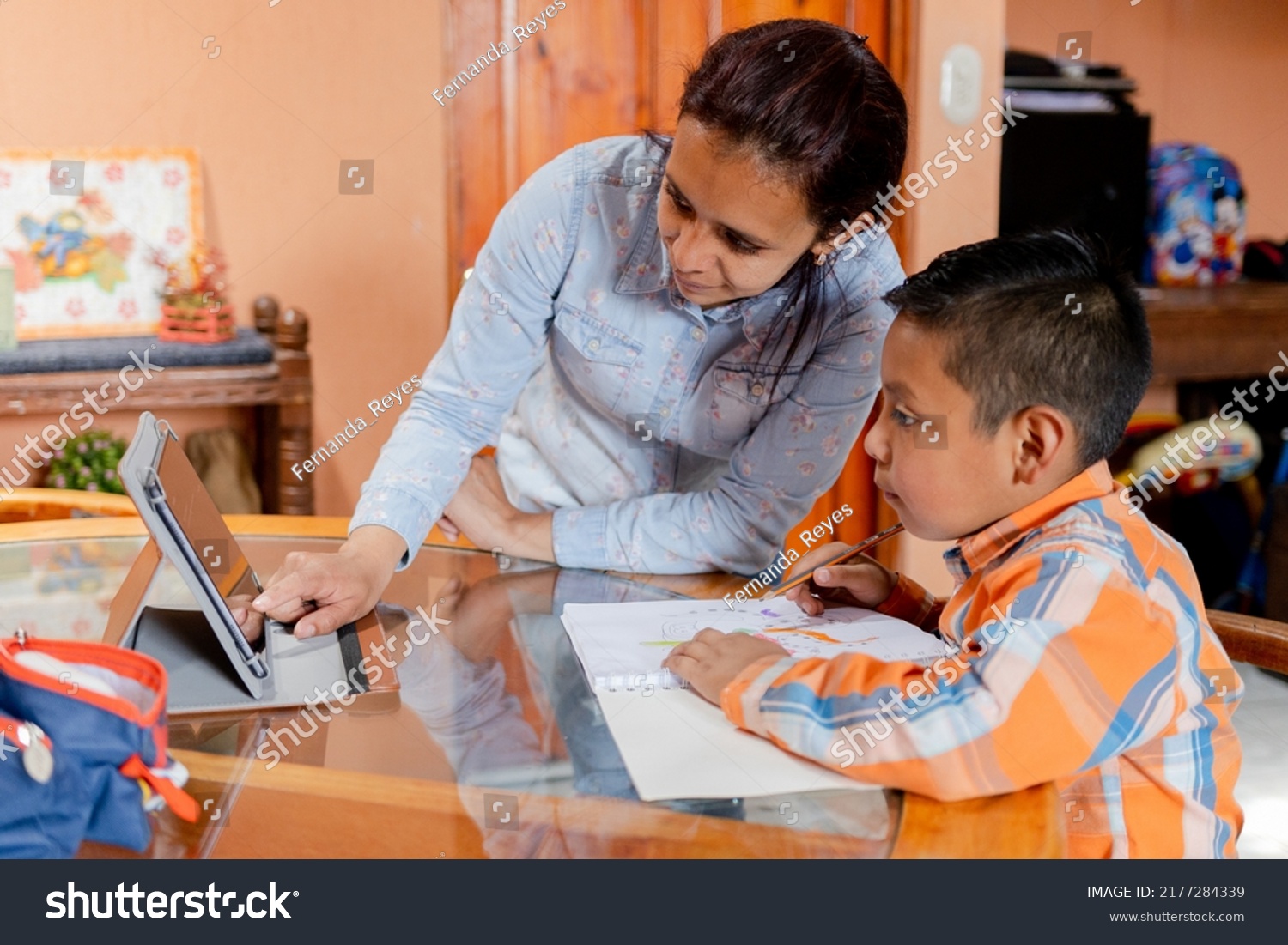 Hispanic mom helping her little son do her homework -homeschooling-young latin mother and her son learn online with tablet at home. #2177284339