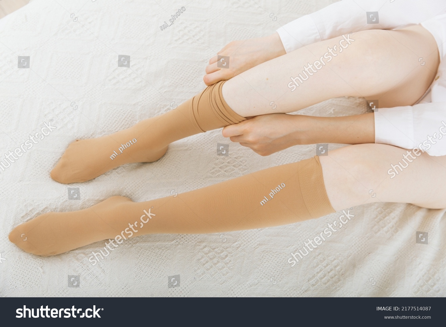 Knee socks or socks. Beige compression stockings on a woman in a white room. Girl putting on stockings at home. Beautiful female legs. #2177514087