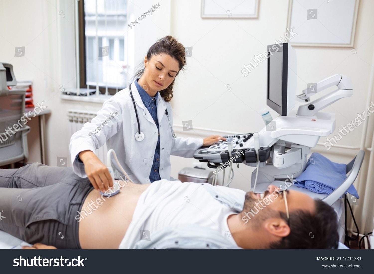 Young male patient lying on bed and having ultrasound examination of abdomen in medical clinic #2177711331