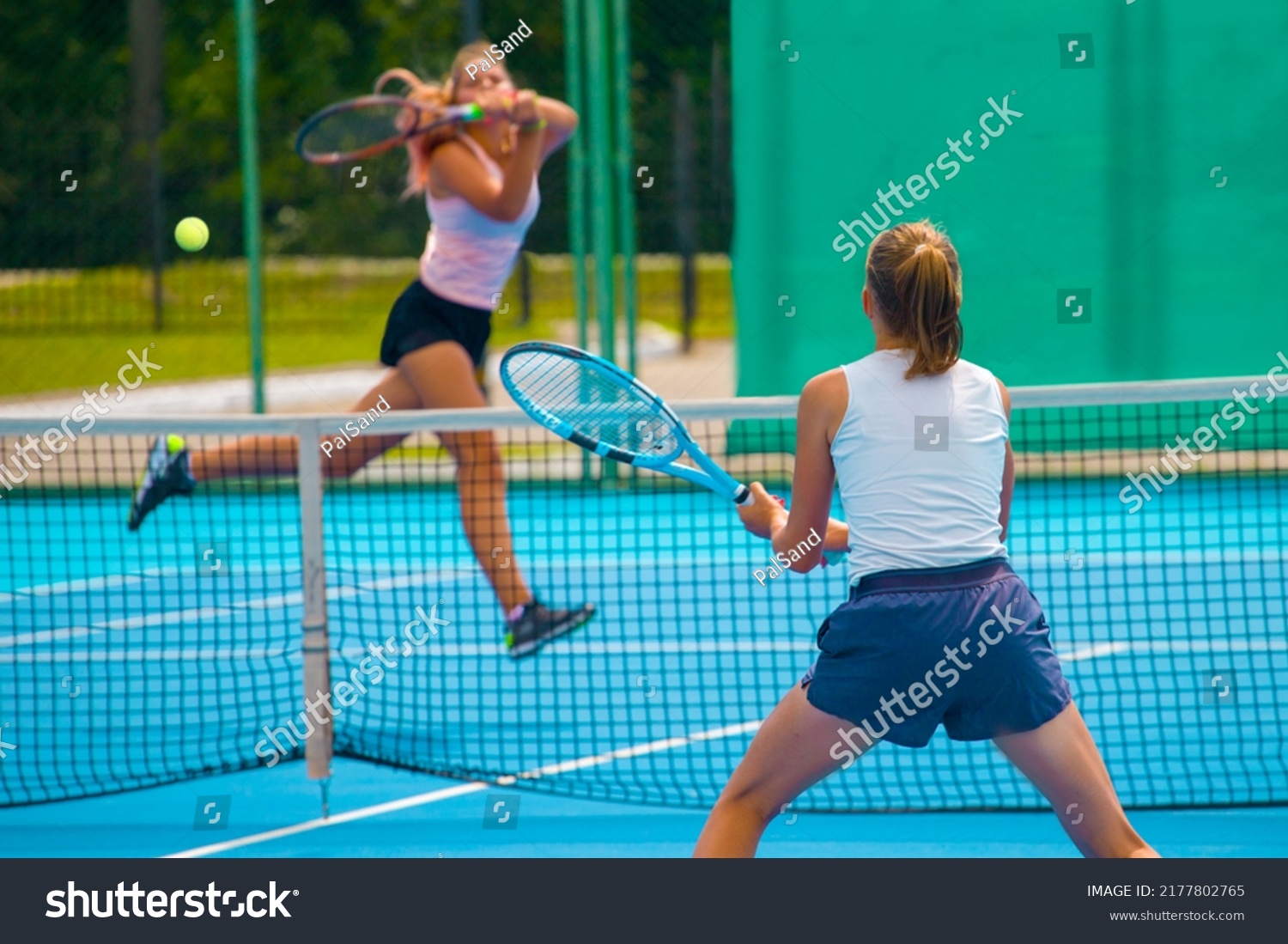 A girl plays tennis on a court with a hard blue surface on a summer sunny day #2177802765