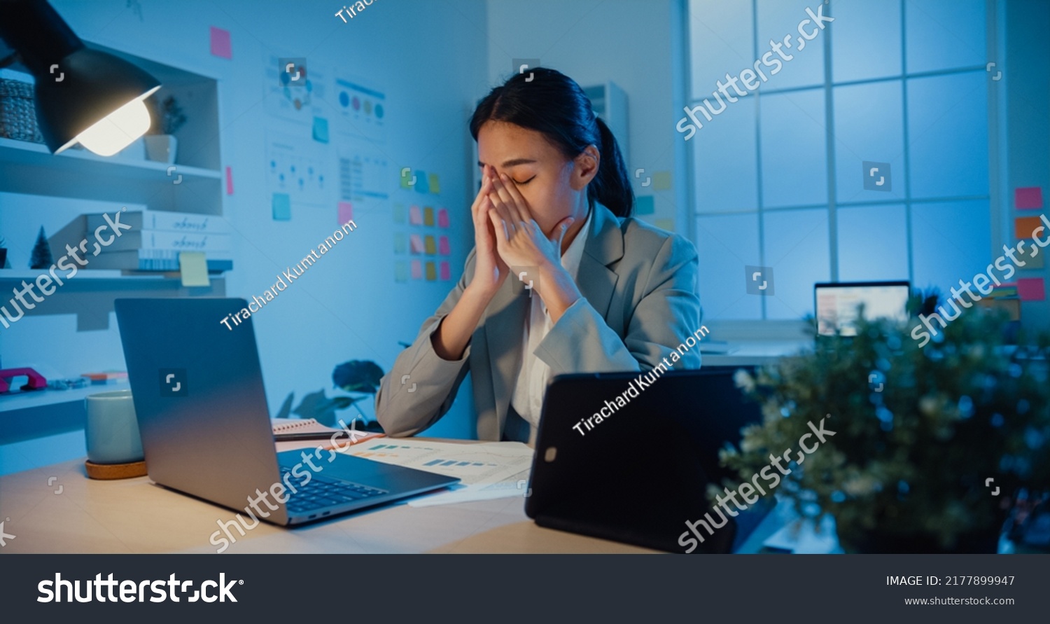 Young Asia businesswoman sit with laptop and tablet on desk rubbing eye feel pain and tired from overwork in office at night. Female suffer of office syndrome long work, Mental Health workplace. #2177899947