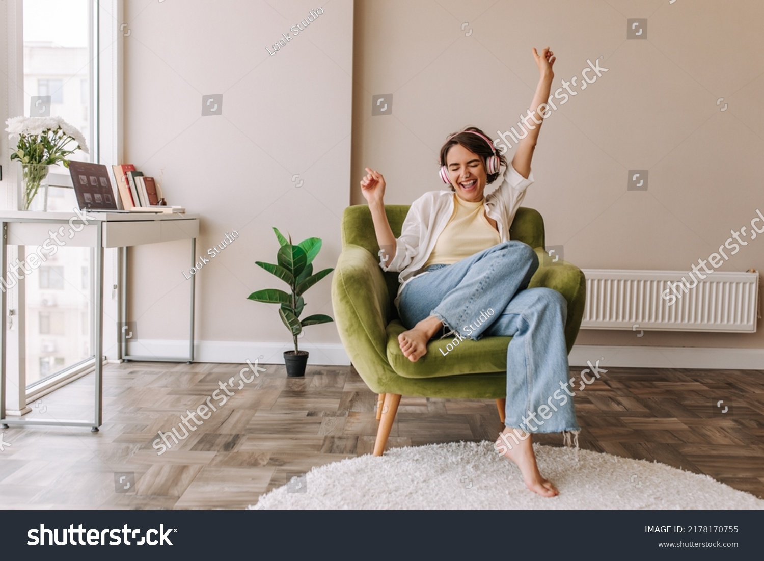 Young pretty woman listening music in headphones . Full view of funny caucasian woman having fun at home sitting on green chair. Concept of use technology  #2178170755