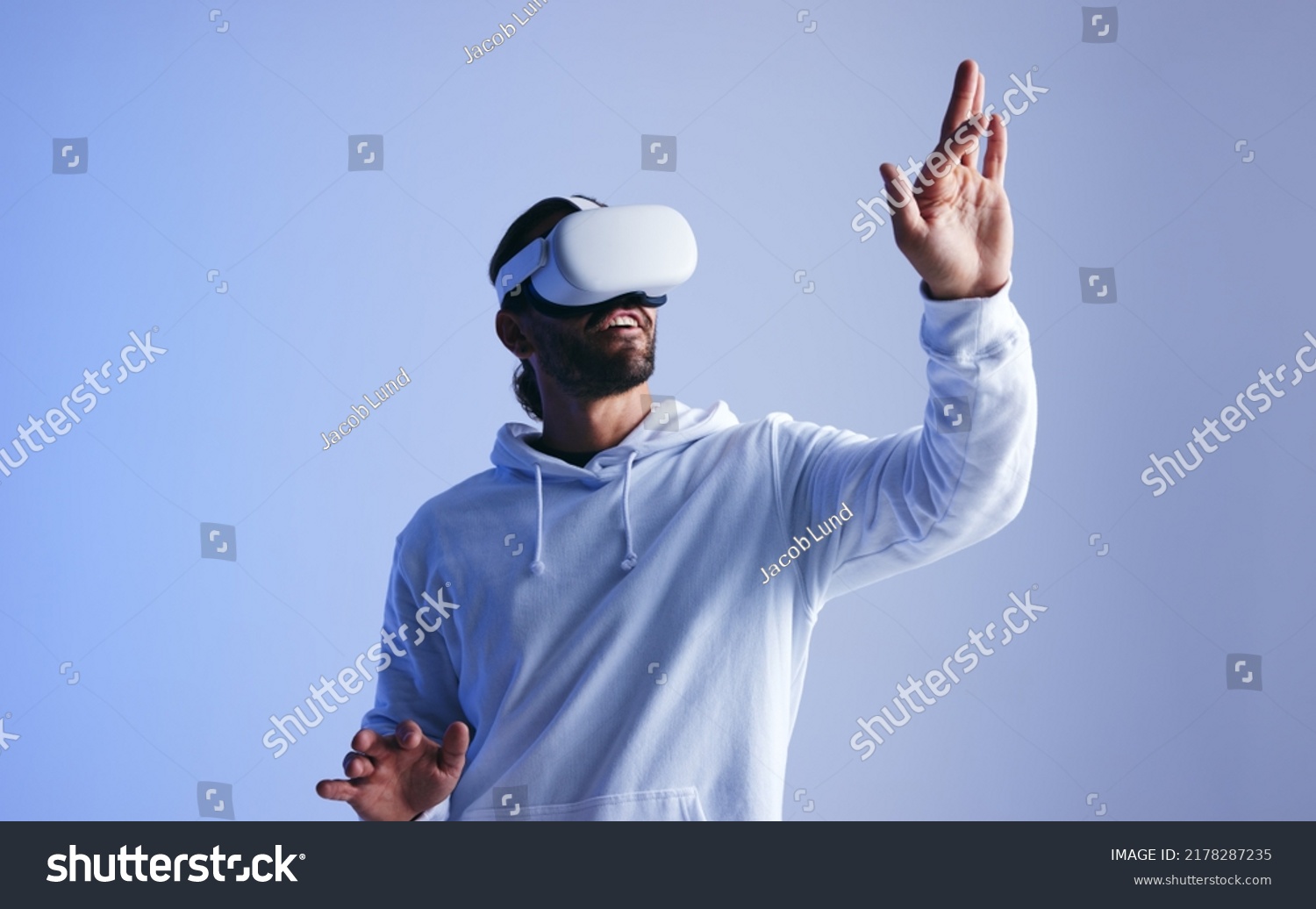 Happy young man touching virtual space with his hand. Cheerful young man experiencing a fun 3D simulation. Young man interacting with the metaverse using virtual reality goggles. #2178287235