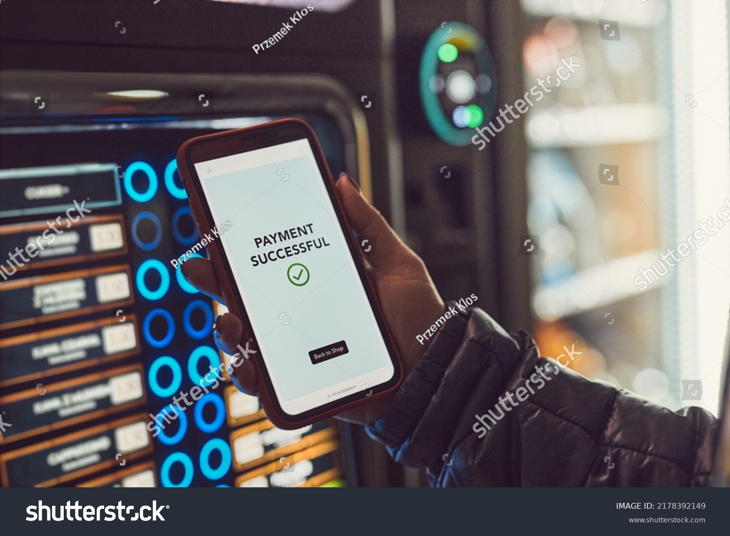 Consumer paying for product at vending machine using contactless method of payment with mobile phone. Woman using payment app on smartphone to buy product. Female hand holding smart phone with pay app #2178392149