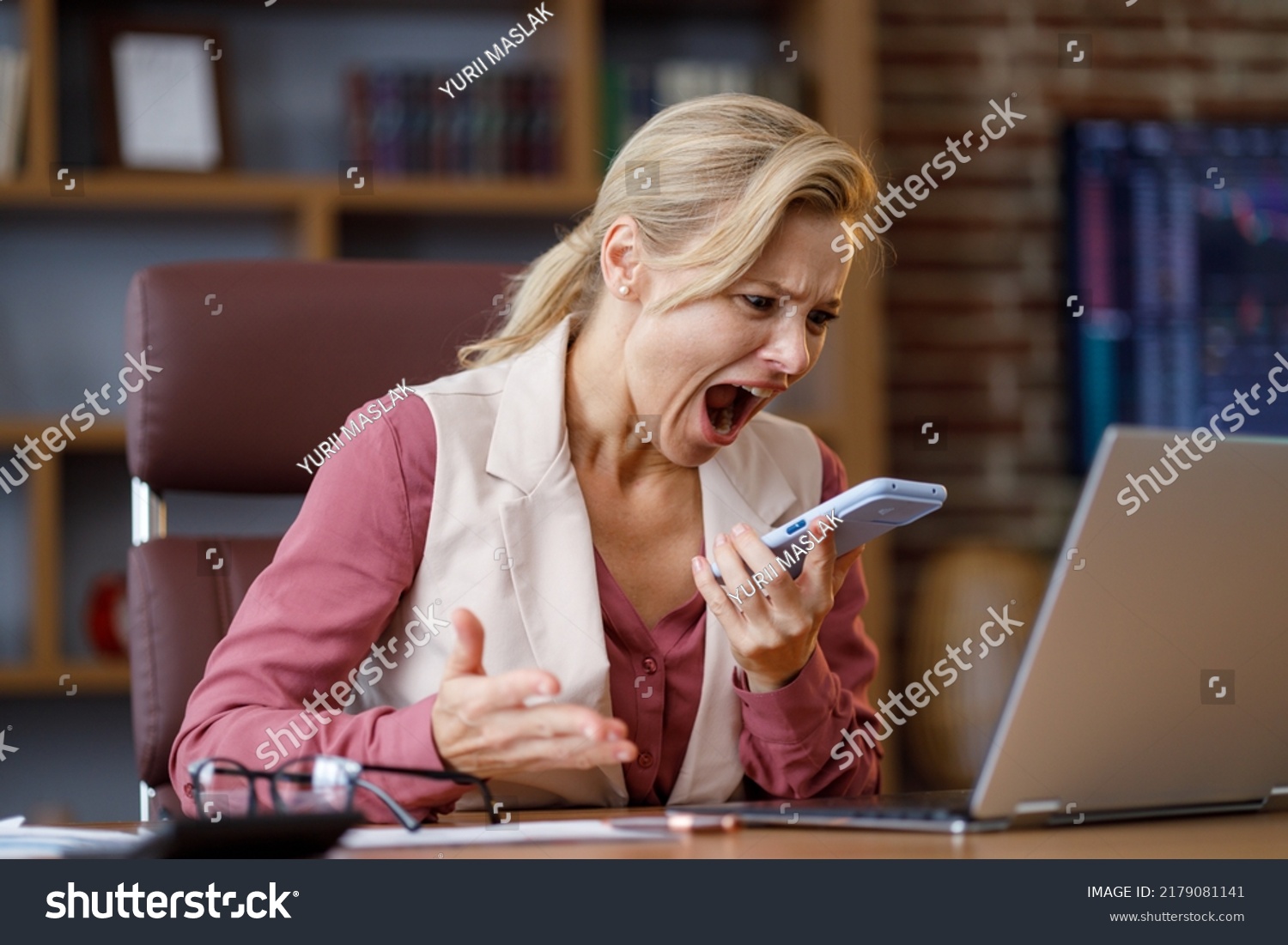 Furious businesswoman shouting expressively to smart phone while answering phone call at office. Angry annoyed woman enraged of bad service, having problem with not working mobile phone, get spam #2179081141