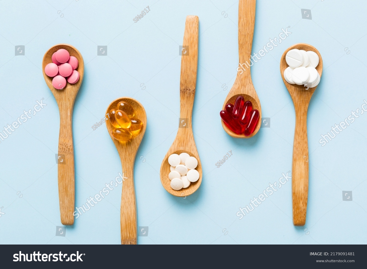 Vitamin capsules in a spoon on a colored background. Pills served as a healthy meal. Red soft gel vitamin supplement capsules on spoon. #2179091481