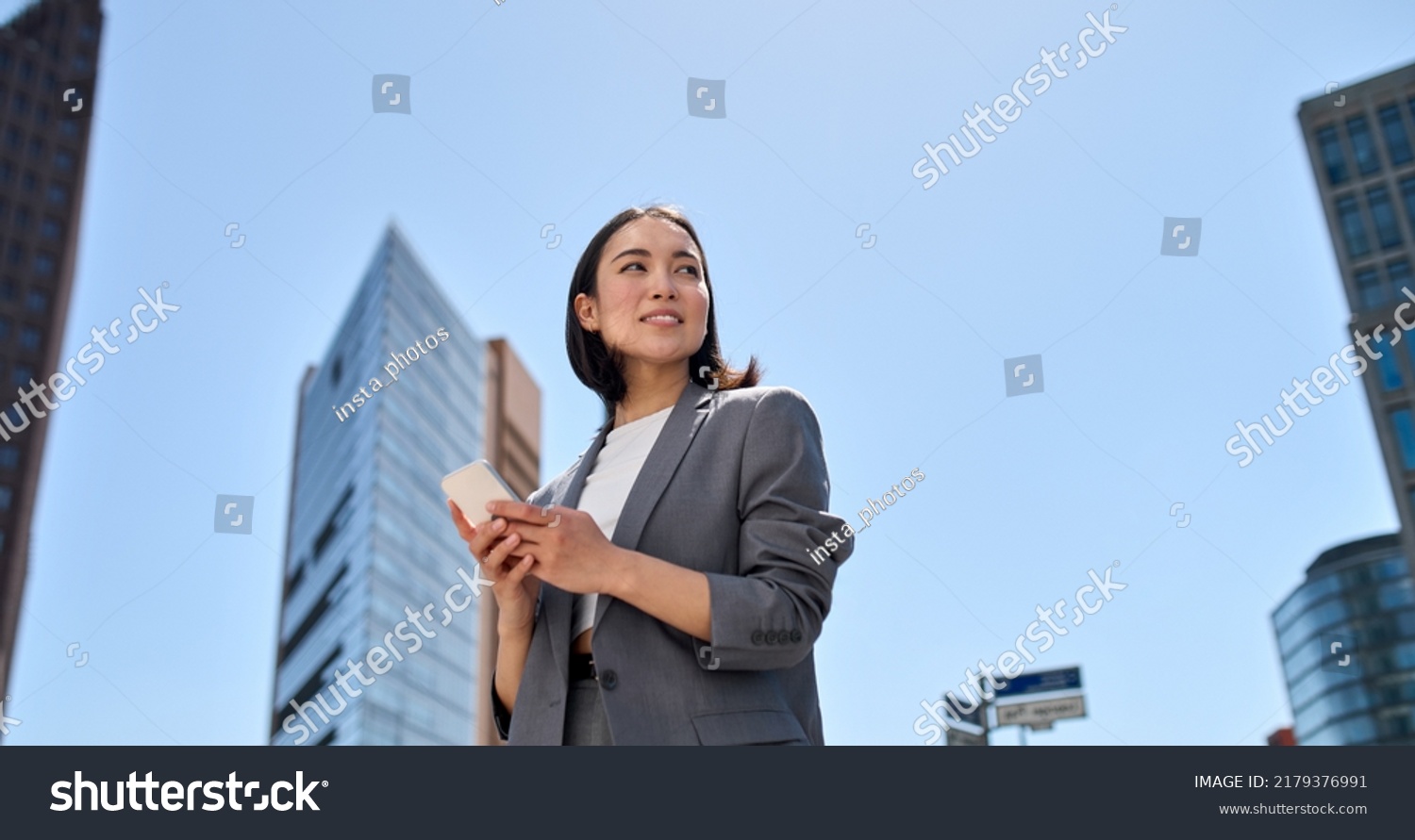 Young busy successful beautiful Asian business woman, korean professional businesswoman holding cellphone using smartphone standing or walking on big city urban street outside. #2179376991