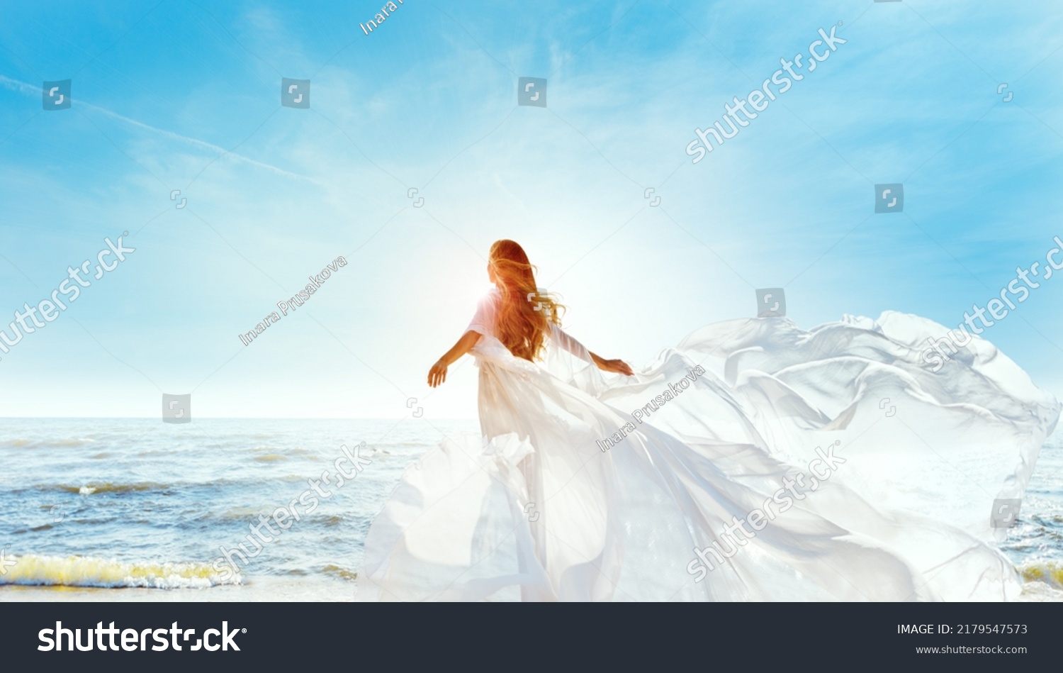 Model in White Dress Flying on Wind. Happy Woman Enjoying Sun looking away at Blue Sky. Carefree Girl dreaming at Sea Beach Resort. Freedom and Spiritual Relax Concept #2179547573