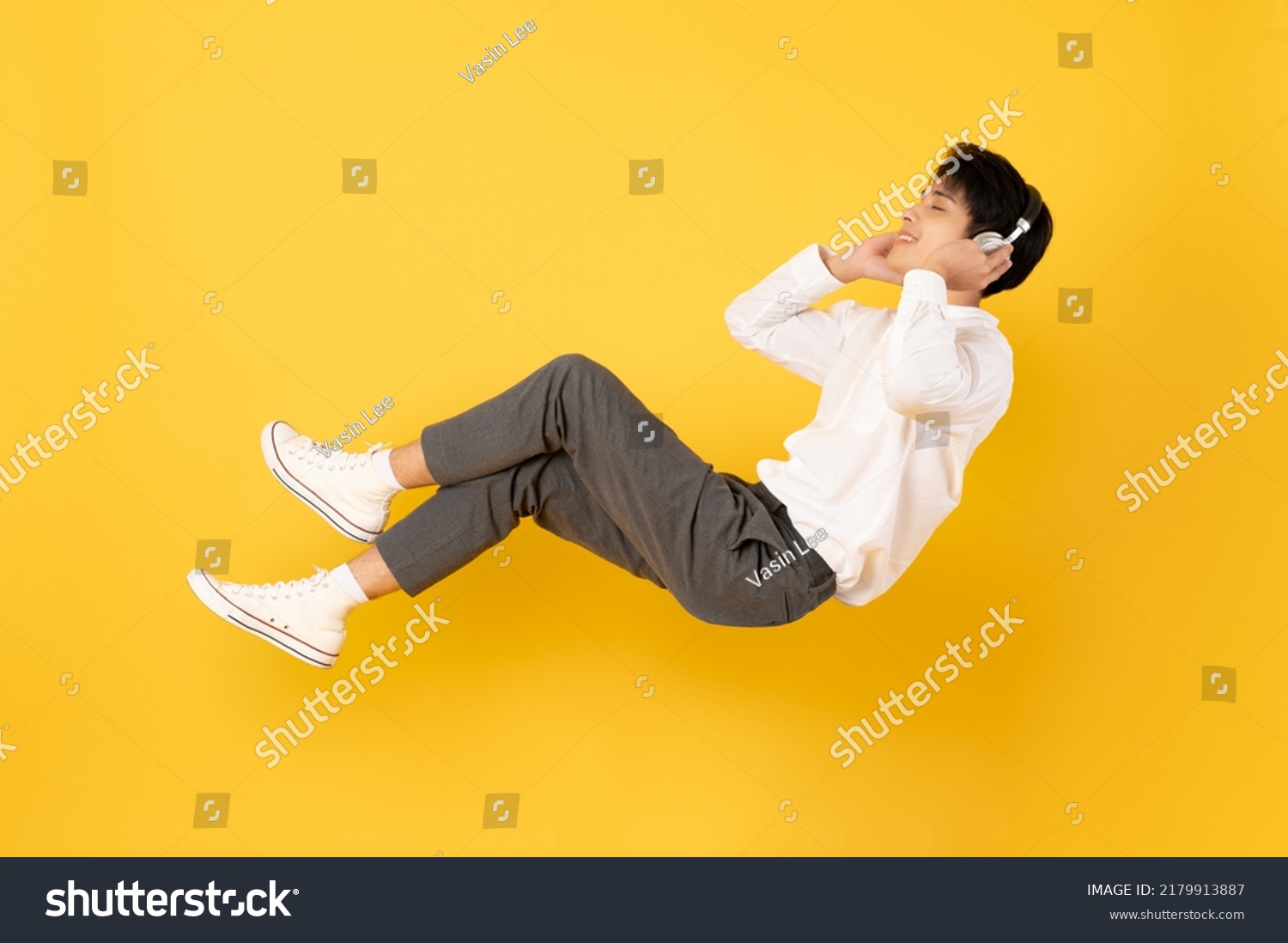 Young good looking asian man floating while listen with headphone isolated on yellow background #2179913887