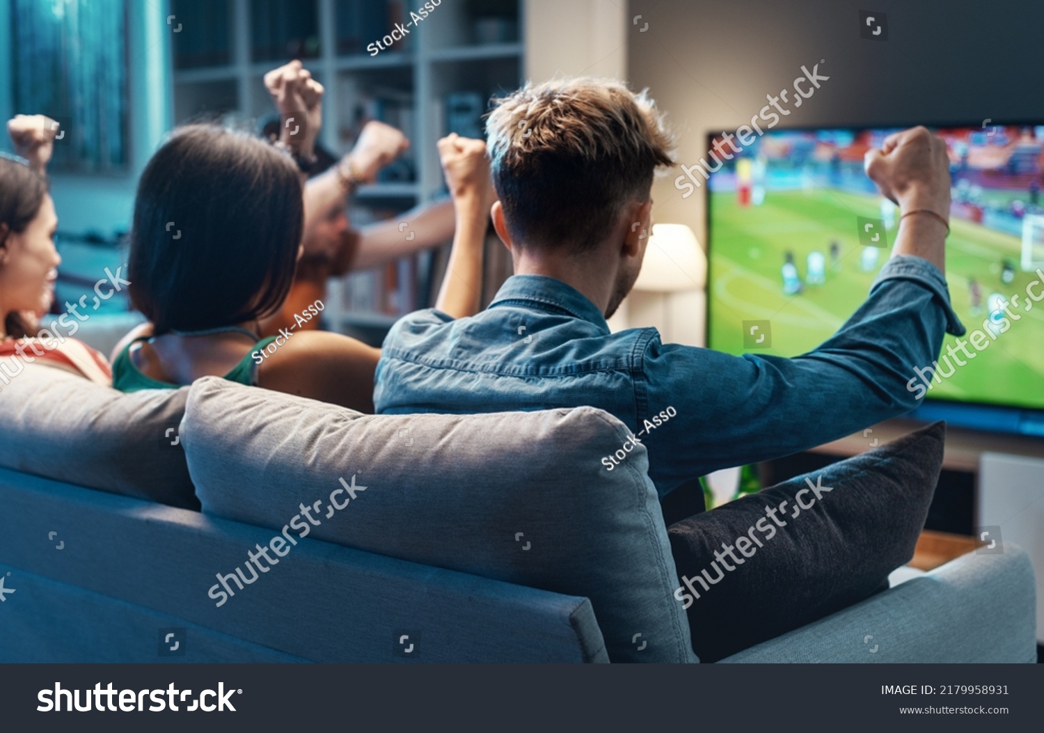 Group of young friends watching a football match on TV together and cheering for their team #2179958931