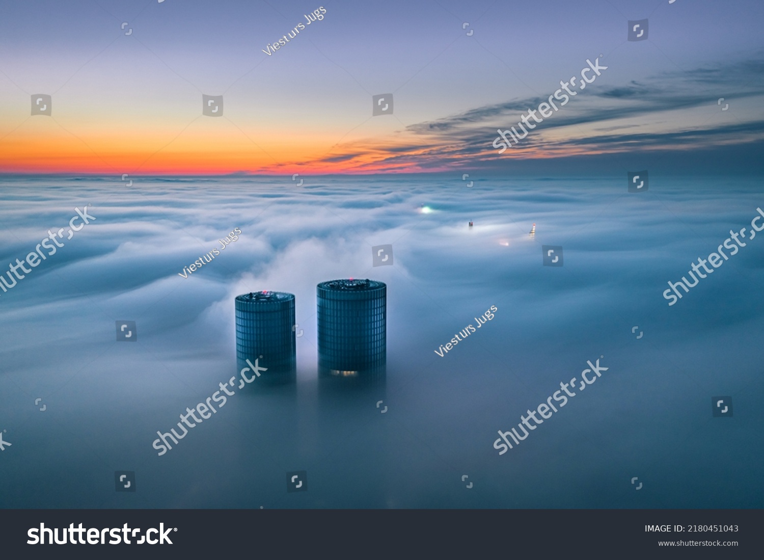 Skyscraper rooftop over the clouds at sunrise. Thick fog covers the Riga city, and warm sunlight over the clouds and church tower. #2180451043