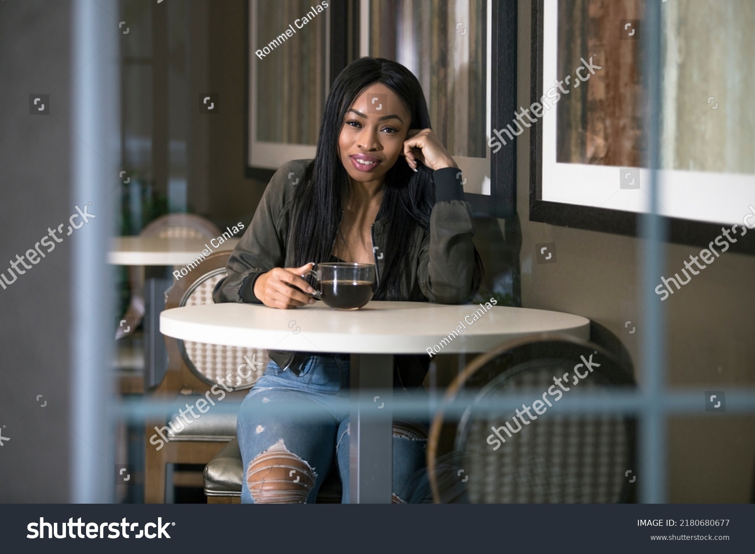 Window view of a black female having coffee in a coffeeshop or sidewalk cafe.  The entrepreneur businesswoman on a break or student is waiting patiently and looks independent. #2180680677