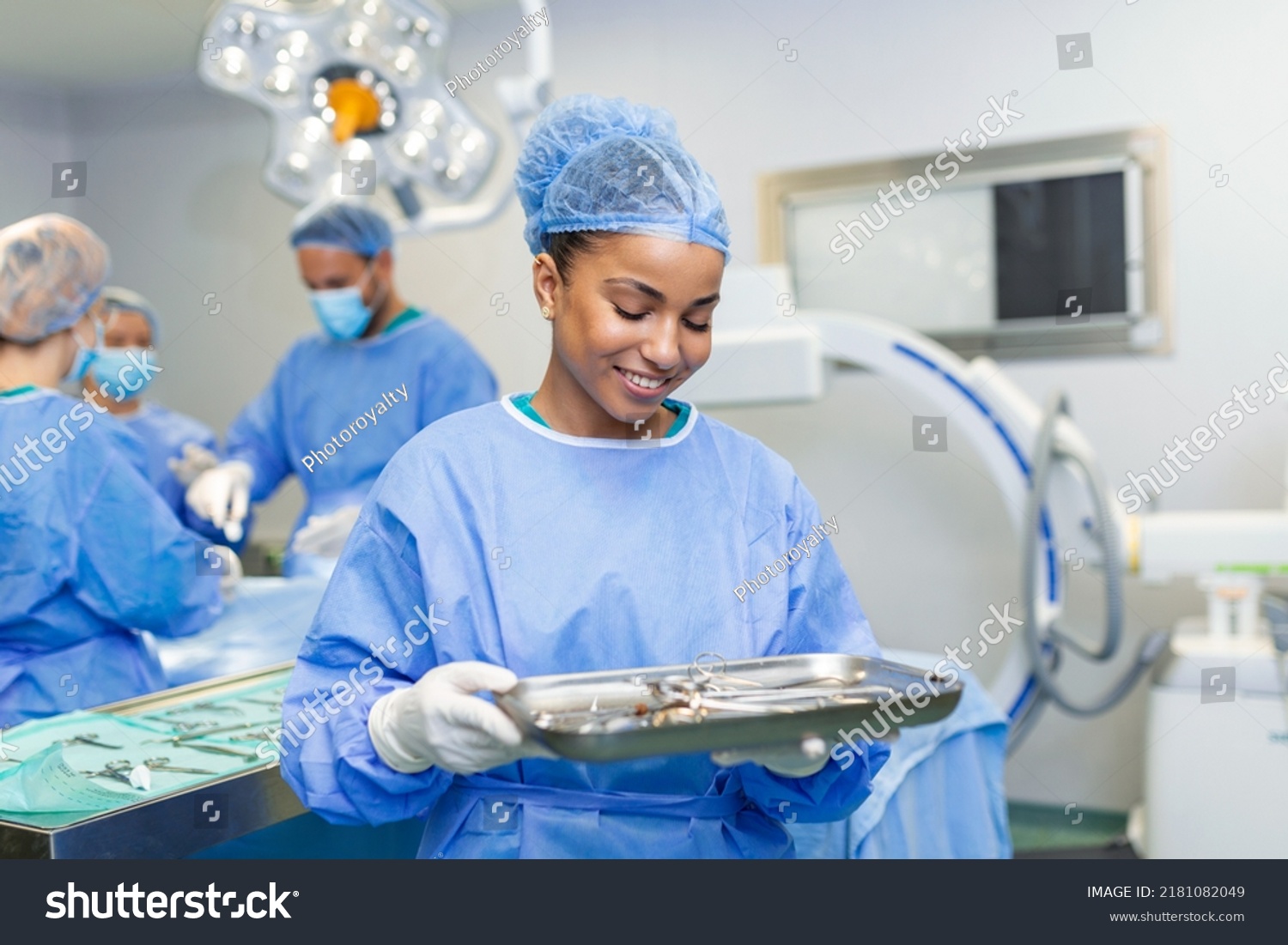 Portrait of female woman nurse surgeon OR staff member dressed in surgical scrubs gown mask and hair net in hospital operating room theater making eye contact smiling pleased happy looking at camera #2181082049