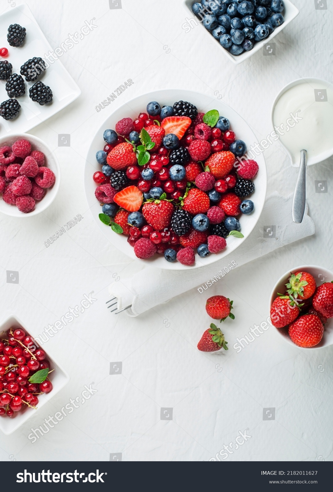 Bowl of healthy fresh berry fruit salad with cream on white background. Top view. Berries overhead closeup colorful assorted mix of strawberry, blueberry, raspberry, blackberry, red currant #2182011627