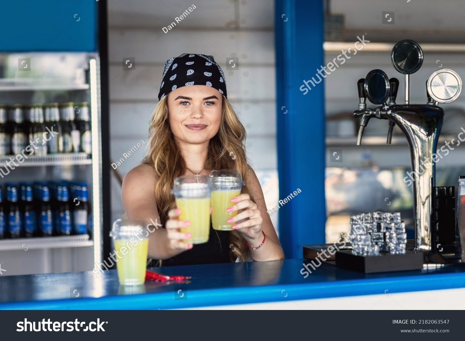 Hipster girl bartender serving fresh lemonade behind counter at outdoor bar during summer festival #2182063547