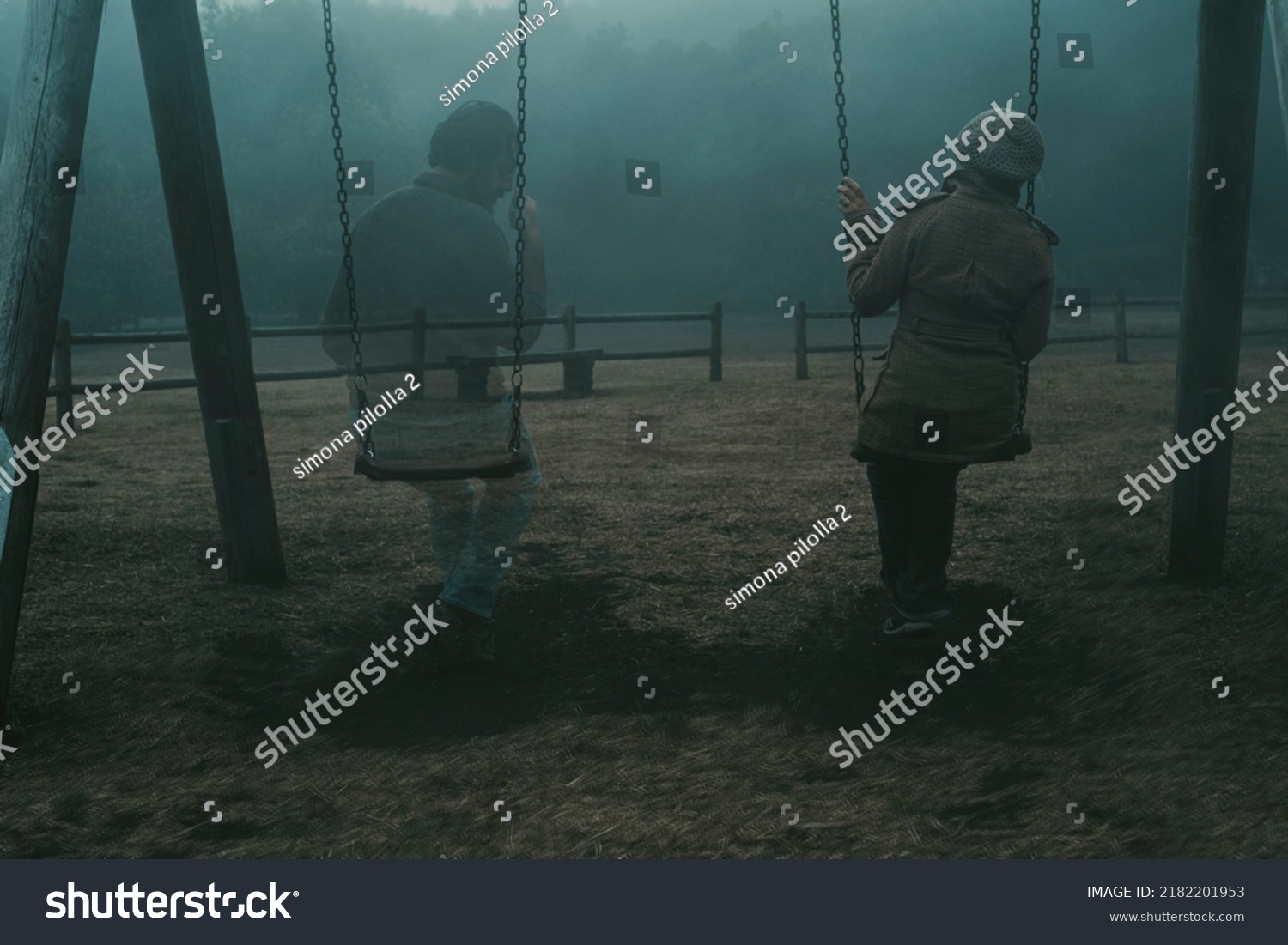 Concept of afterlife and memory for parents or lost love. Back view of woman sitting on a swing with ghost man near her outdoor in the park with fog. . Dead friend or husband concept. Life and death #2182201953