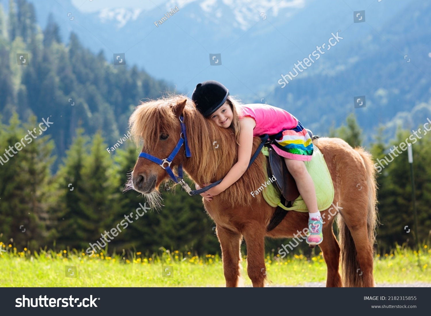 Kids riding pony in the Alps mountains. Family spring vacation on horse ranch in Austria, Tirol. Children ride horses. Kid taking care of animal. Child and pet. Little girl in blooming meadow. #2182315855
