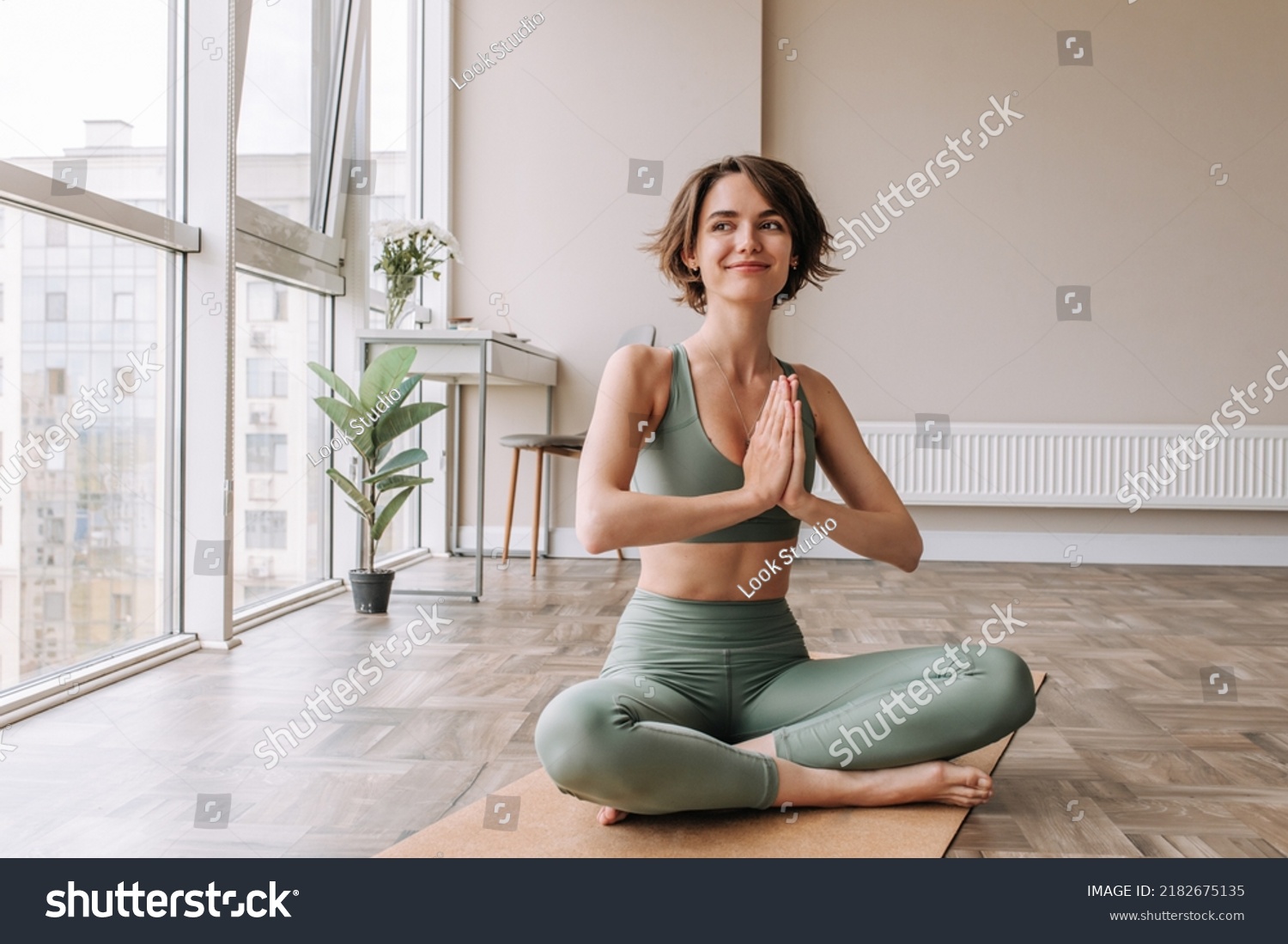 Pretty young brunette woman practicing yoga at home . Caucasian cute girl looking away and smiling wearing green sportswear sitting on the floor. Concept of leisure, relaxation, workout  #2182675135