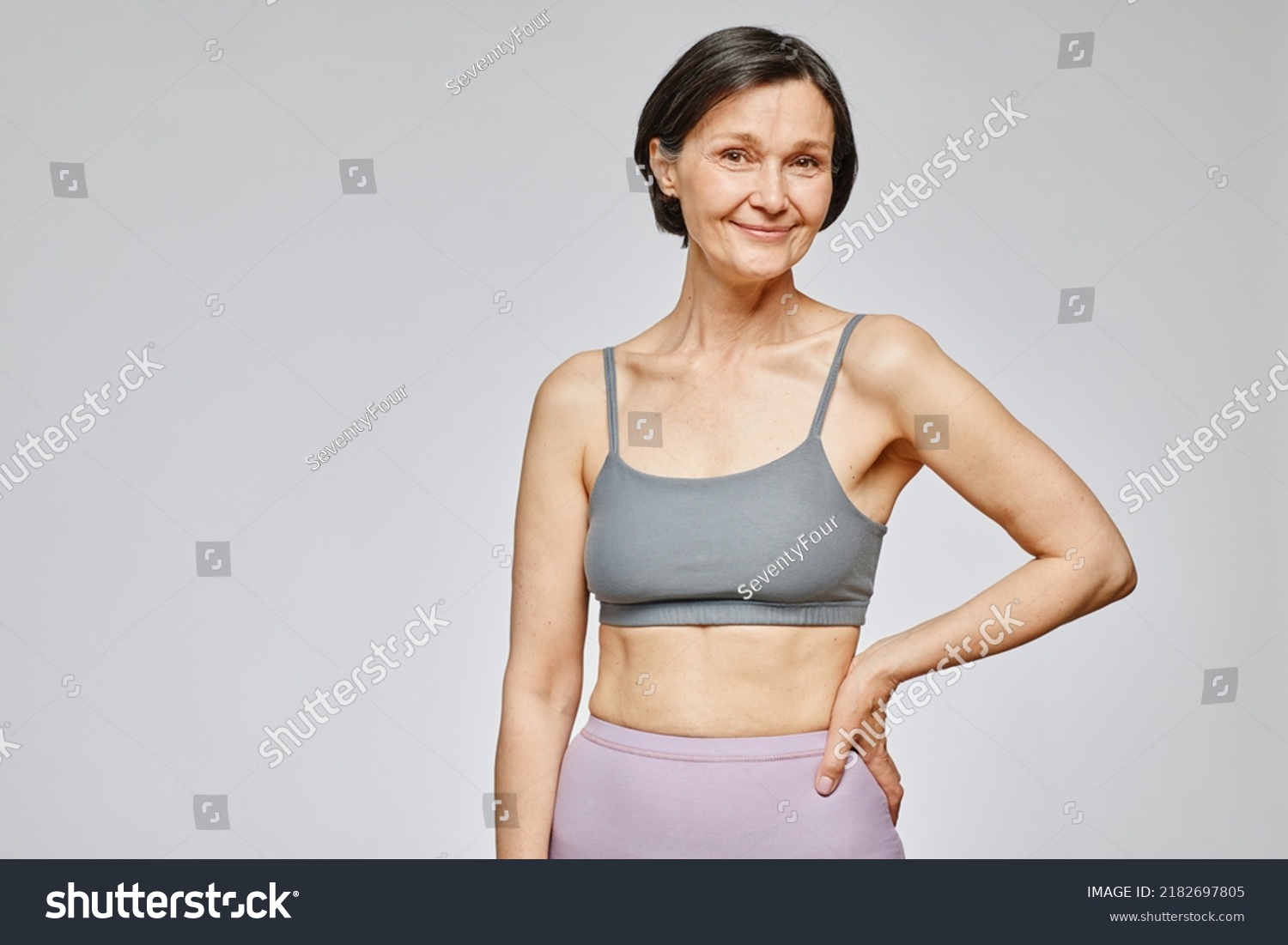 Minimal waist up portrait of smiling mature woman wearing neutral underwear against grey background, body positivity concept, copy space #2182697805