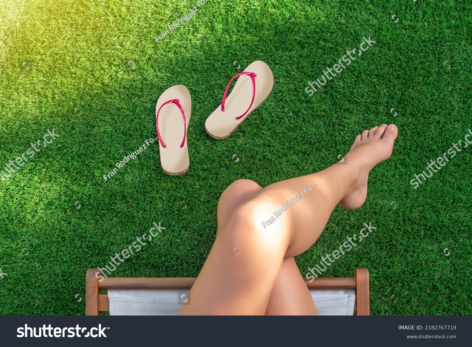 Selective focus of a girl sitting in a hammock on artificial turf with bare feet and flip-flops on the grass #2182767719