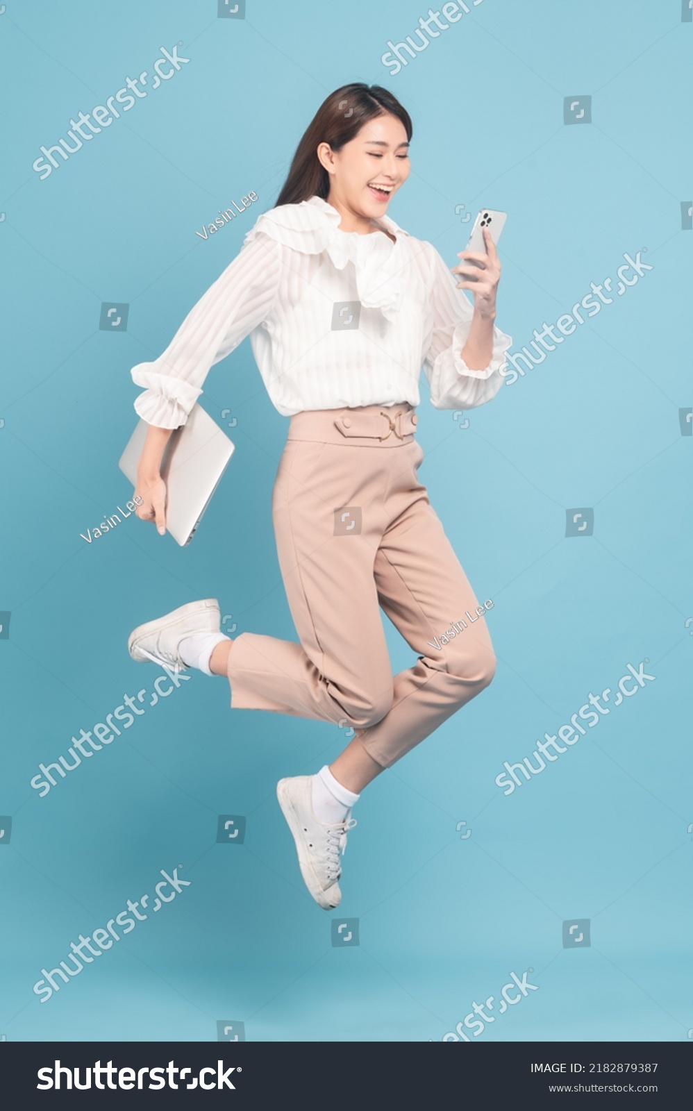Young beautiful asian woman with smart casual cloth use smartphone and jump isolated on blue background #2182879387