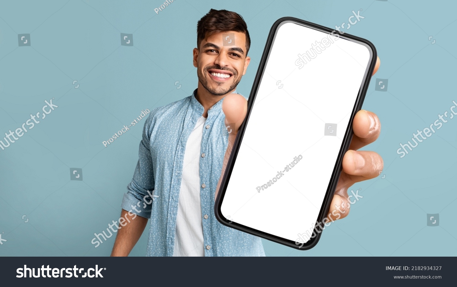 Smiling Handsome Arab Guy In Casual Showing Mobile Phone With White Blank Screen For Advertisement, Recommending Mobile Dating Application, Panorama With Free Space, Mockup, Colllage #2182934327