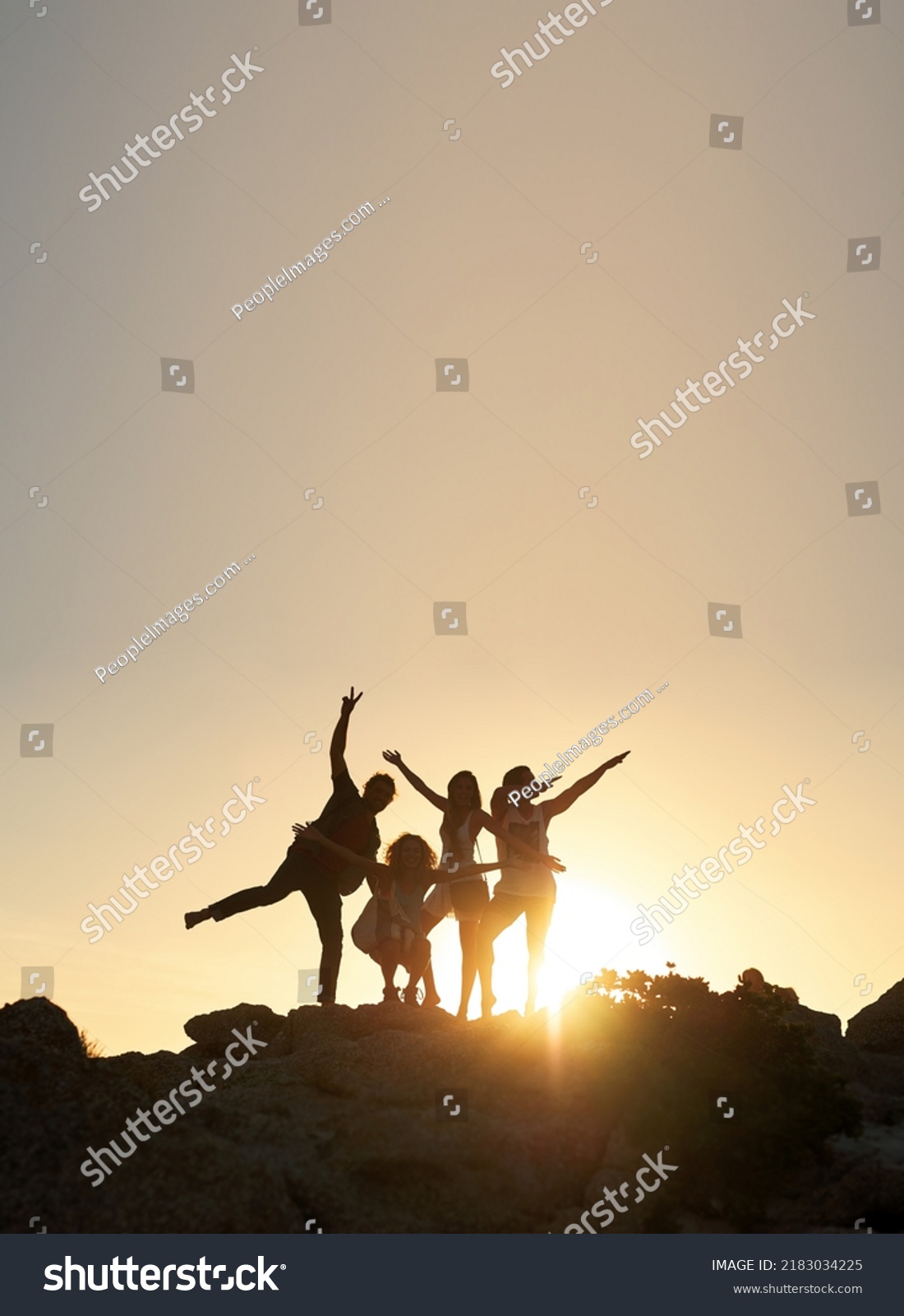 Group of friends posing standing on rocks at sunset having fun summer vacation lifestyle celebrating friendship #2183034225