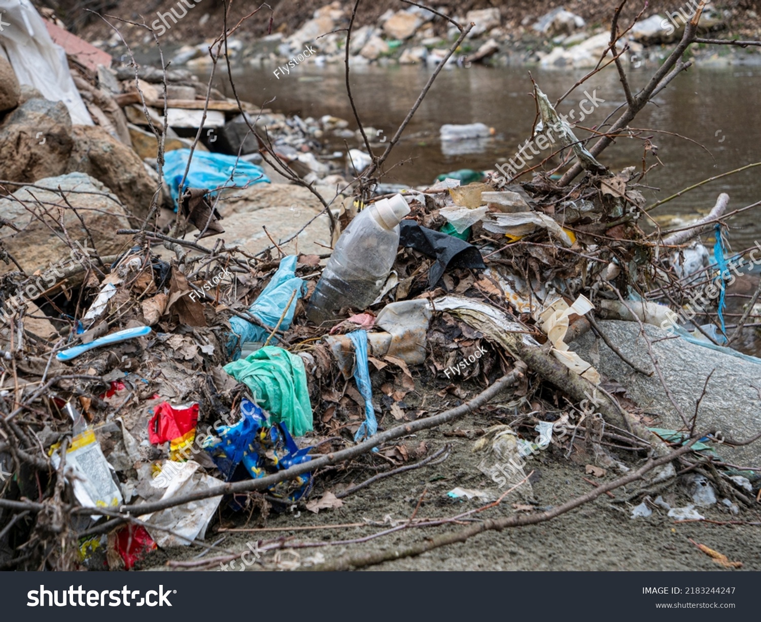 TIRANA, ALBANIA, MARCH 2022: Flooded plastic rubbish at the river bank as waste management issue. River debris and plastic garbage mix on a sandy river shore. The need to raise environmental awareness #2183244247